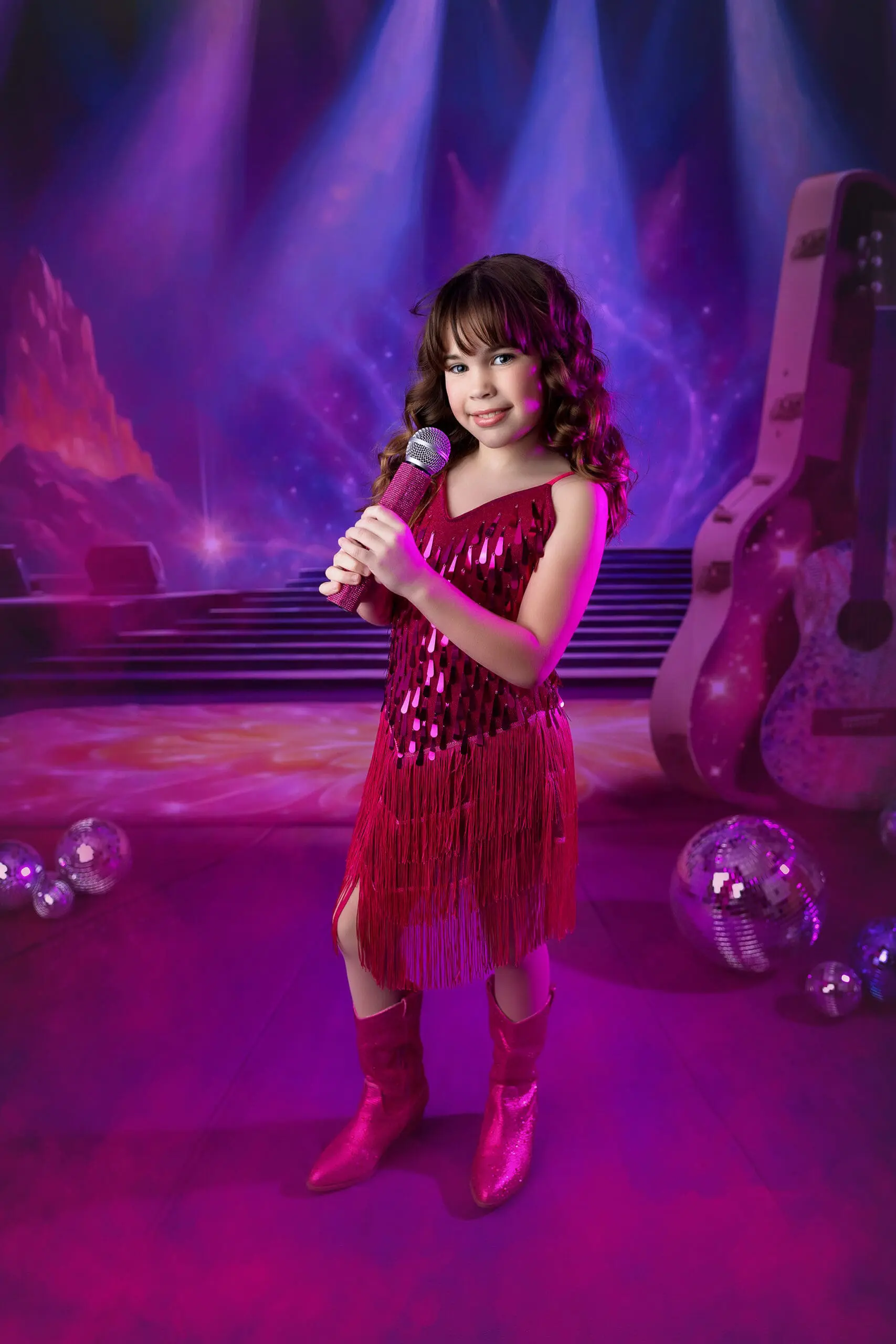 Young girl in a sparkling red fringed dress and matching boots holds a microphone on a stage. The background features a large guitar, disco balls, and colorful lights, creating a festive, musical atmosphere. Fun Taylor Swift inspired session for a girl in Milford Connecticut