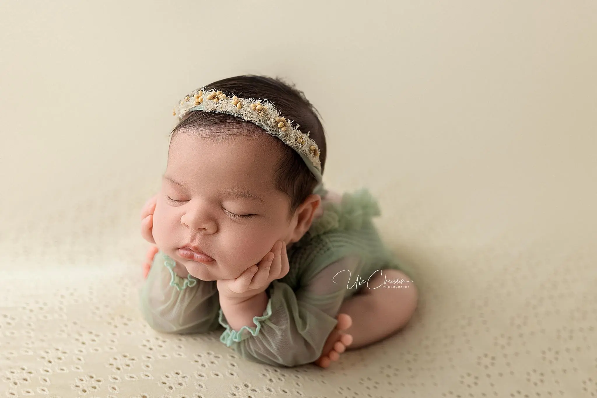 A sleeping baby wearing a floral headband and a green outfit, with their head resting on their hands. Midwives in Connecticut often capture these serene moments, showing the little one lying on a light-colored, textured surface.