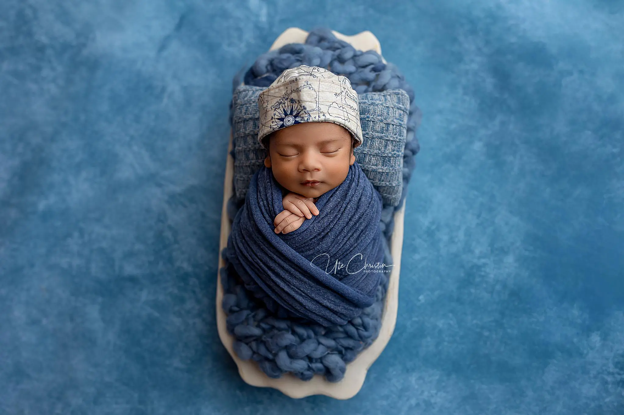 A newborn baby is swaddled in a dark blue blanket, wearing a light patterned cap, and lying peacefully on a blue textured background—ready for sweet dreams or perhaps their first baby music classes in CT.
