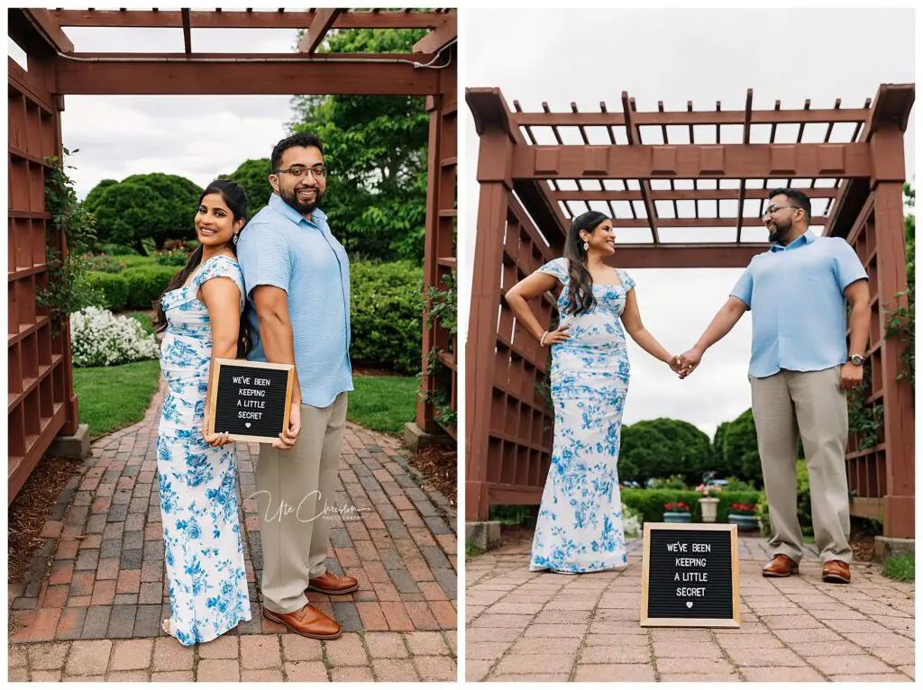 A couple stands in a garden under a wooden arbor, holding hands and smiling. The woman holds a sign that reads, We’ve been keeping a little secret. Their joy shines as they celebrate with help from Connecticut Fertility Clinic. Both are dressed in blue and white.
