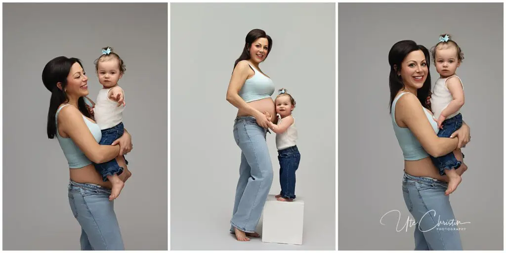 A smiling pregnant woman in a blue crop top and jeans poses with a young girl in matching jeans and a white top. They stand together in a studio, showing affection and happiness.