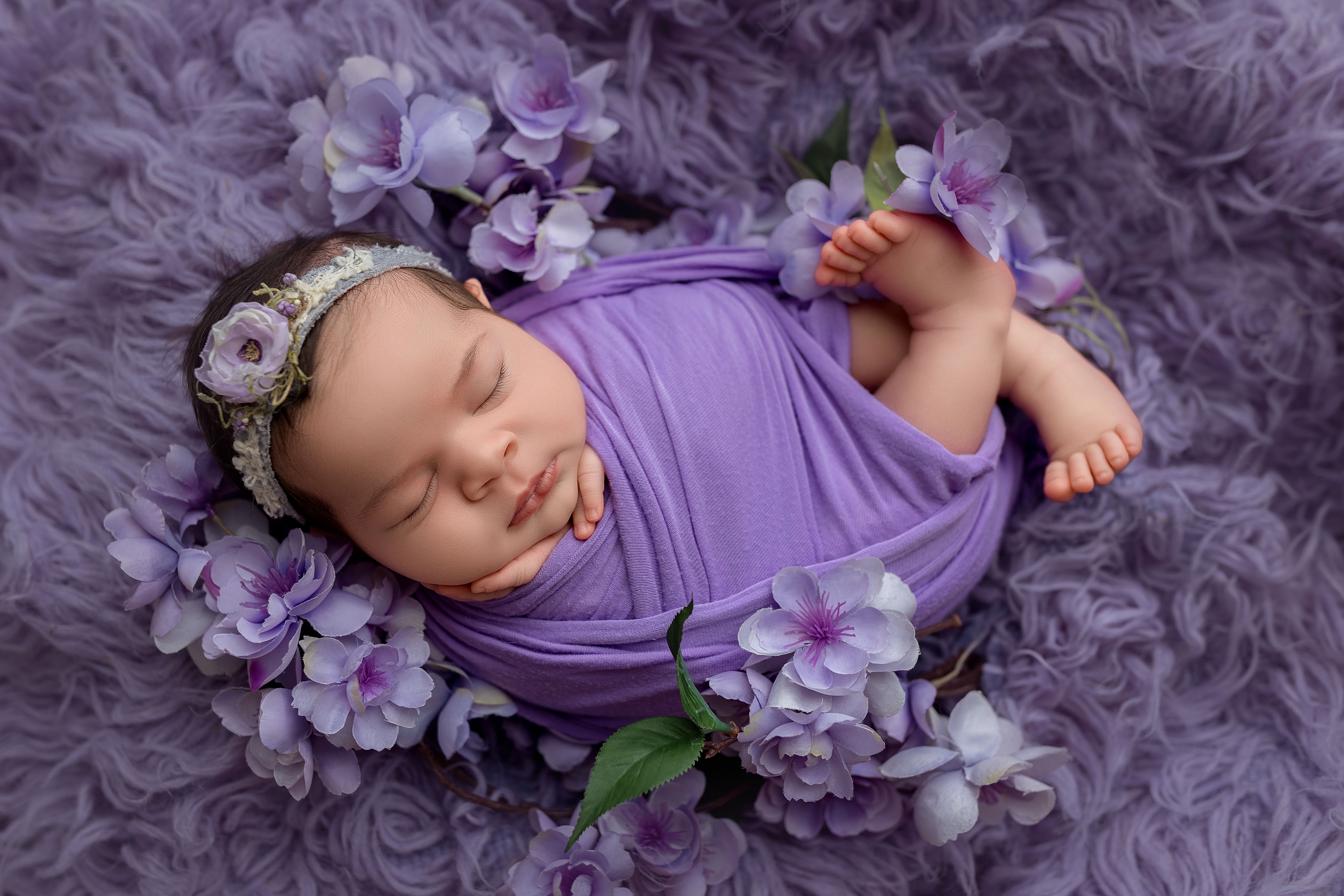 newborn baby girl swaddled in a purple wrap posed in a flower basket for newborn photos