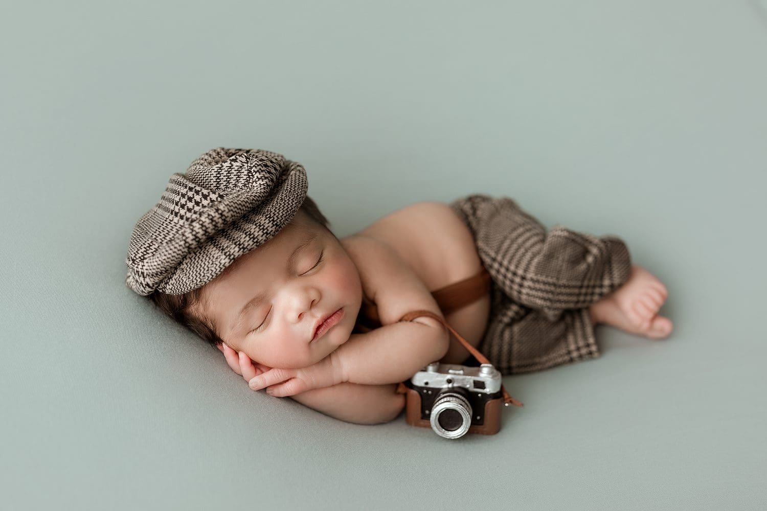 newborn baby holding a camera prop while being photographed