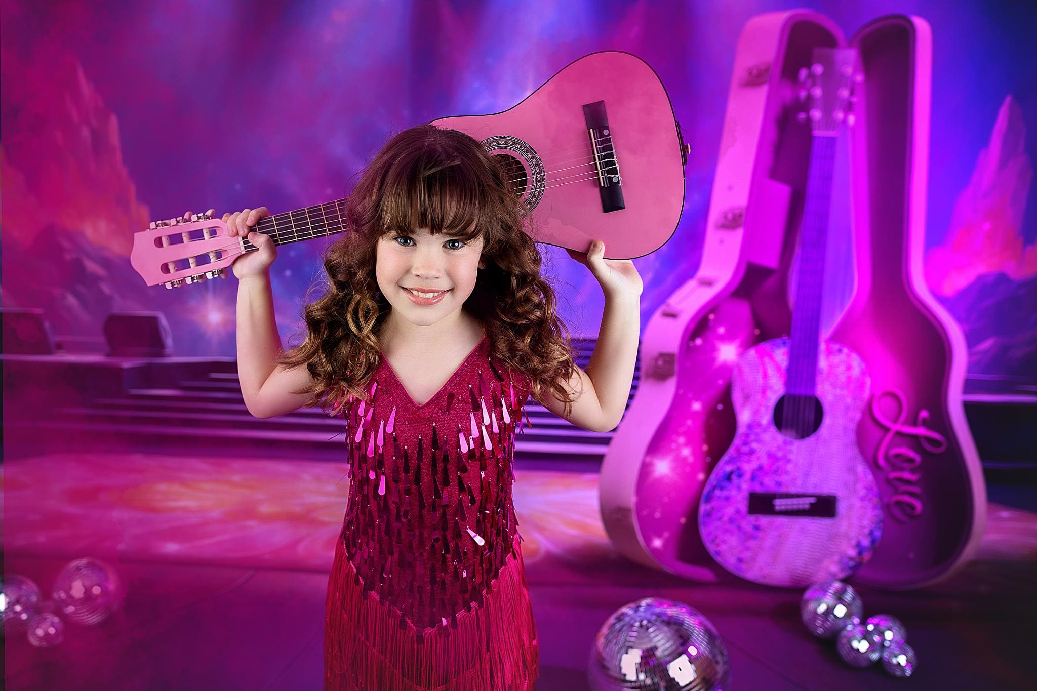 A young girl with curly hair in a pink dress smiles while holding a pink guitar over her shoulders. The backdrop, reminiscent of child photos in Connecticut, features a stage with pink and purple lighting, glittery guitar cases, and disco balls sparkling above.